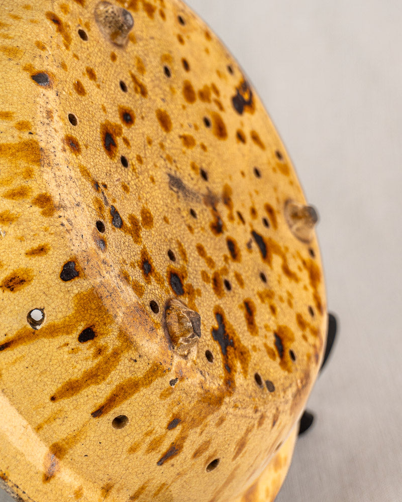 Underside view of 19th-century French earthenware fruit strainer with yellow glaze, brown speckles, and drainage holes.