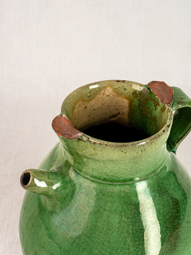 Antique French green-glazed terracotta gargoulette with round body, spout, handle, and vintage wear.