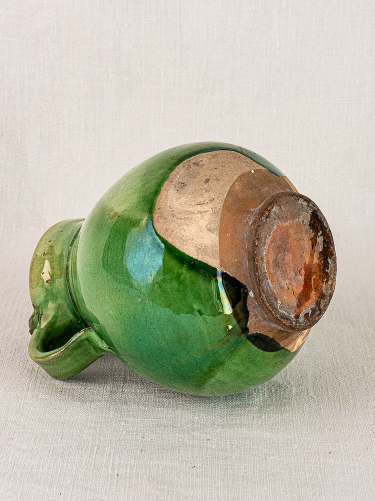 Antique French green glazed terracotta gargoulette shown side-on with unglazed, textured base on neutral fabric.