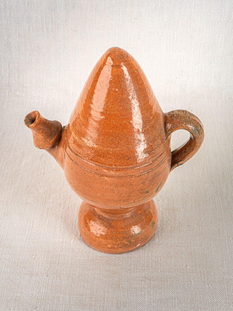Antique French mammiform jug in brown glazed terracotta with handle and short spout on textured surface.