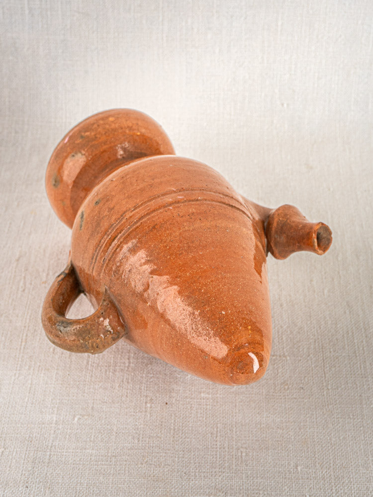 Antique French mammiforme terracotta jug with brown glaze, handle, and spout displayed on textured fabric.