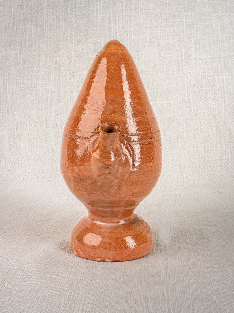 Antique French mammiforme glazed terracotta jug with glossy reddish-brown finish on neutral fabric background.