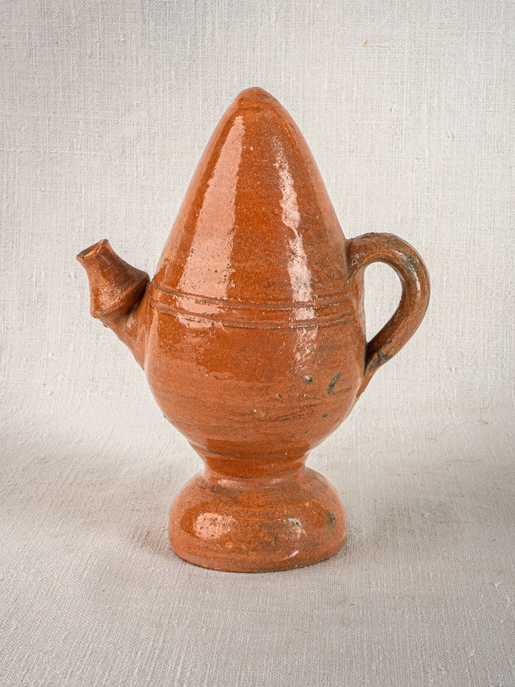 Antique French mammiforme terracotta jug with handle and short spout on light textured surface.