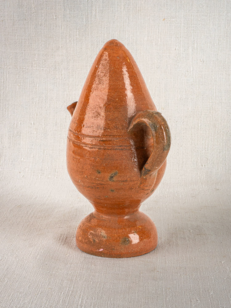 Antique French mammiforme jug in glazed terracotta with two side handles on a textured background.