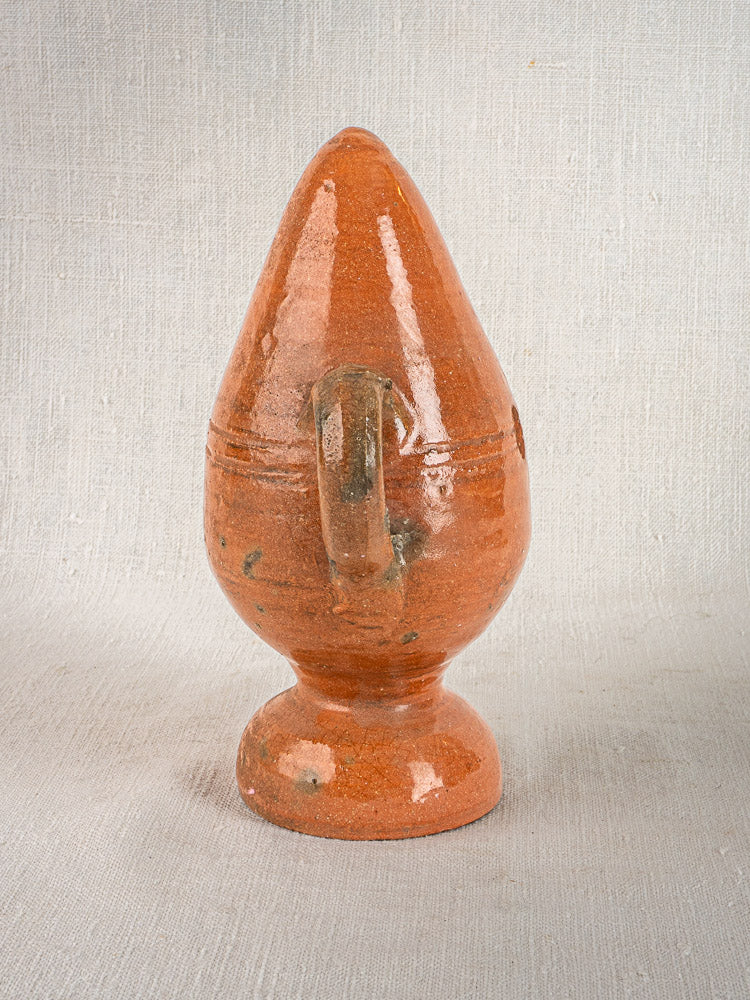 Antique French glazed terracotta mammiforme jug with side handle on a light gray textured surface.