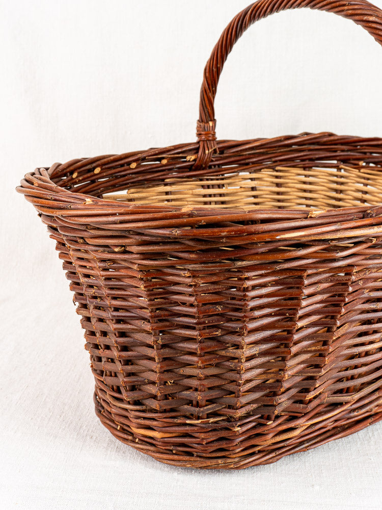 Antique French willow gathering basket, circa 1900, with sturdy handle, displayed on light fabric.