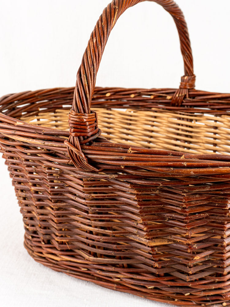 Antique French gathering basket, circa 1900, with woven handle and two-tone brown willow, on a light surface.