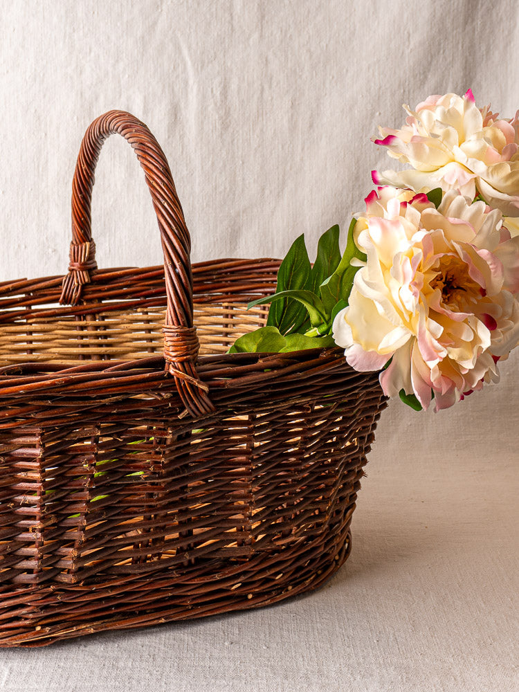 Antique French two-tone willow gathering basket with handle, filled with pale pink and white peonies and green foliage.