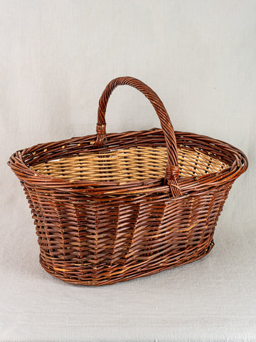 Antique French gathering basket circa 1900 in two-tone willow with handle, displayed on light fabric surface.