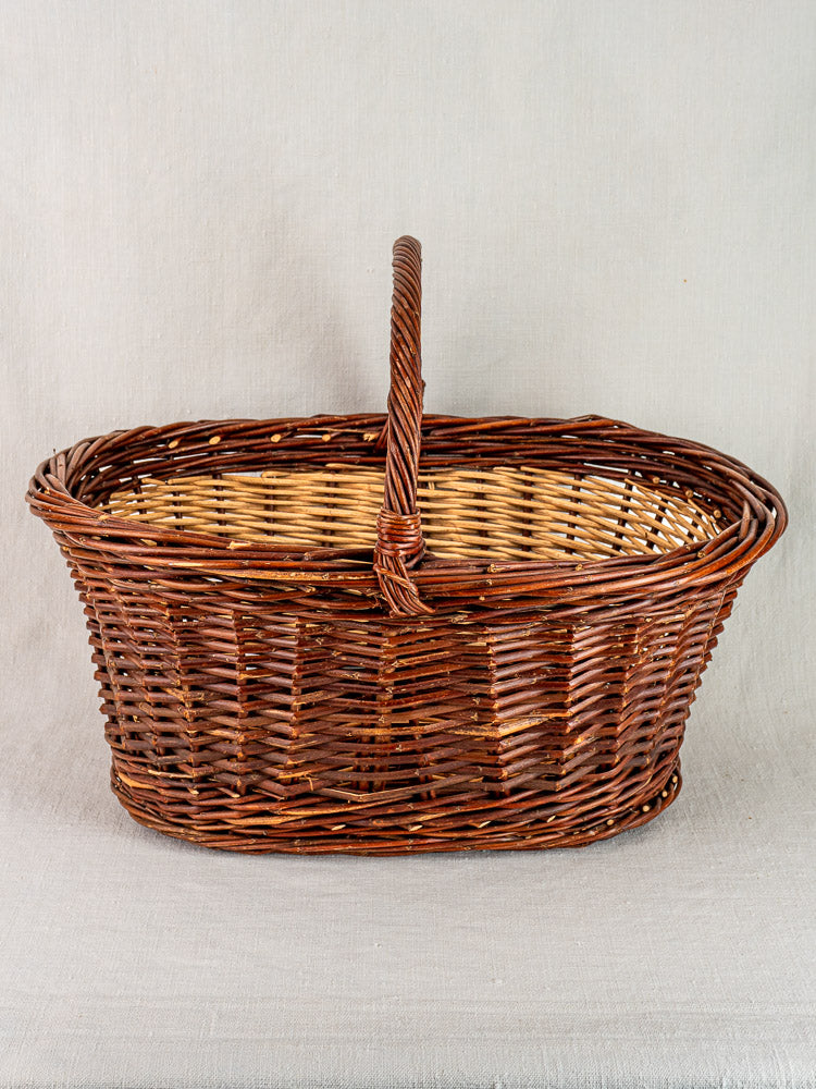 Antique French gathering basket, circa 1900, with brown and beige willow, on light gray fabric surface.