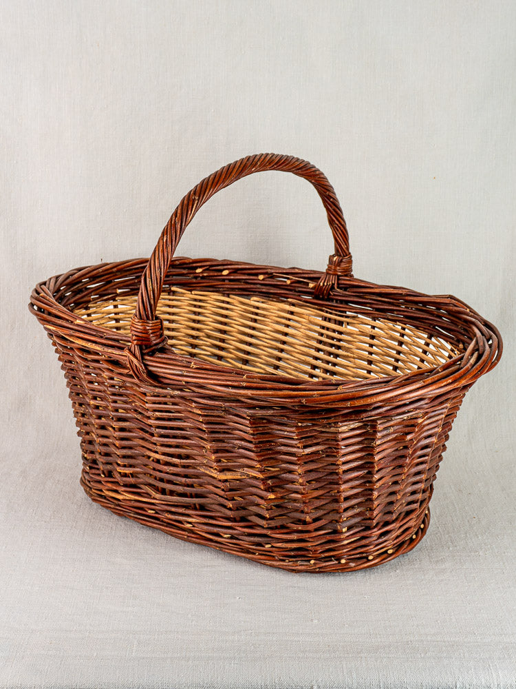 Antique French gathering basket, circa 1900, two-tone willow weave and curved handle on light gray fabric.