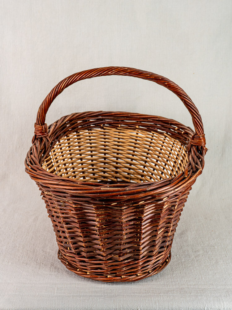 Antique French gathering basket, circa 1900, two-tone willow with sturdy handle, upright on light fabric.