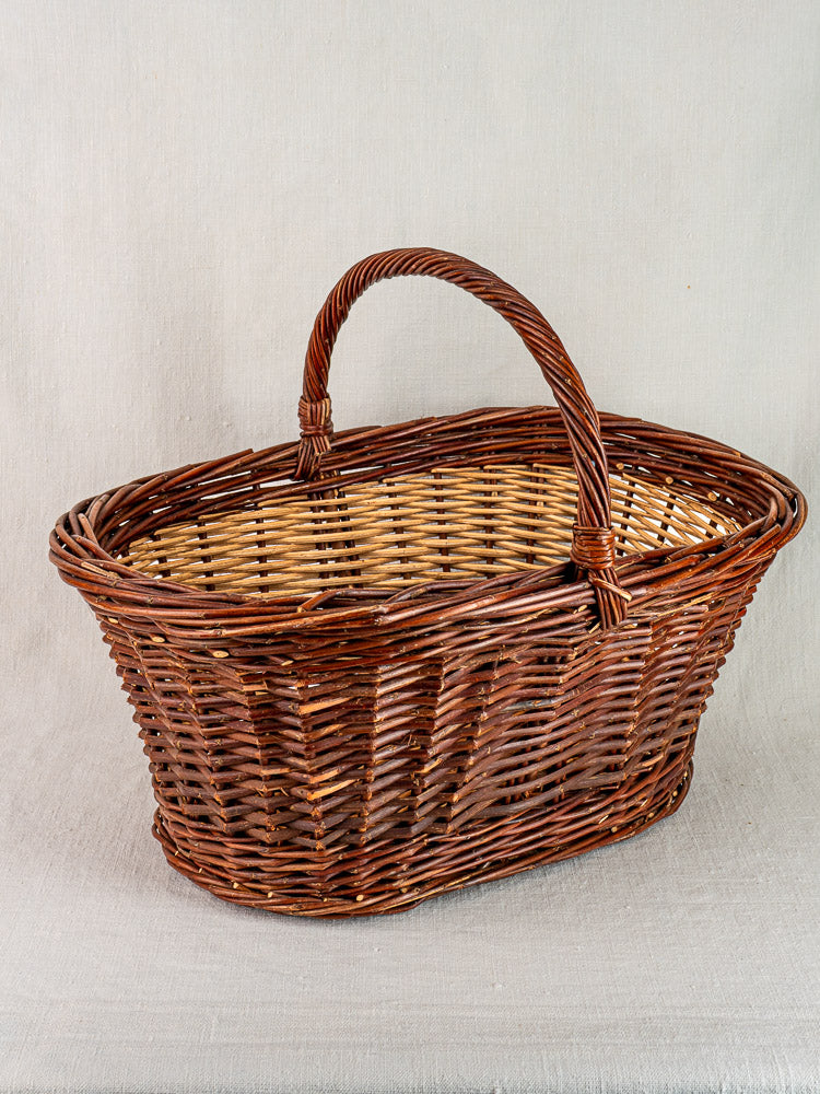 Antique French gathering basket, circa 1900, two-tone willow and handle on light grey textured surface.
