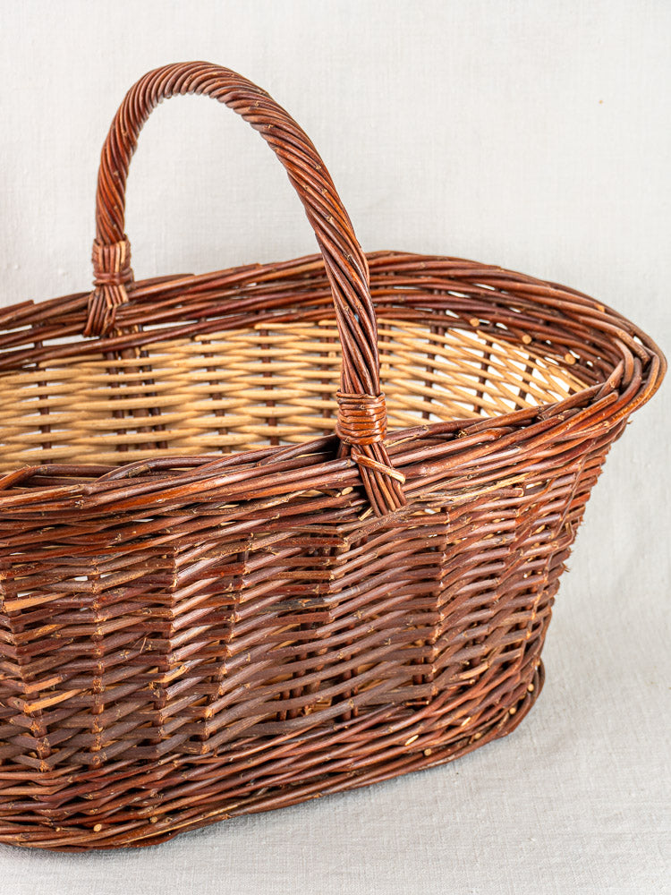 Antique French gathering basket, circa 1900, two-tone willow with sturdy handle on pale fabric background.