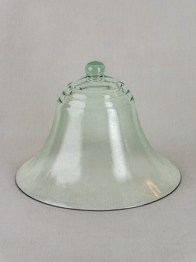 Antique French glass cloche, 19th-century hand blown bell shape with round knob, on plain gray background.