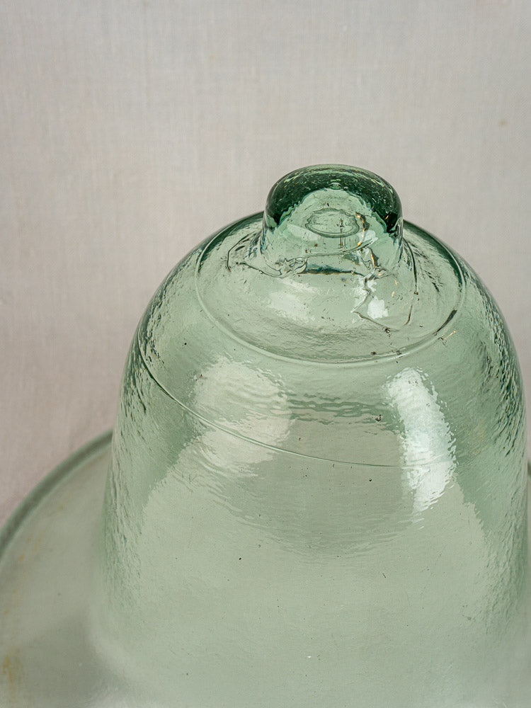 Antique French hand-blown glass melon cloche with clear, green-tinted surface and rounded knob on neutral backdrop.