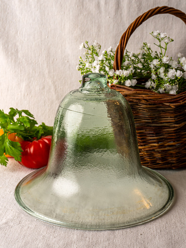 Antique French hand-blown glass melon cloche on linen, with white flowers, bell peppers, and fresh green herbs nearby.