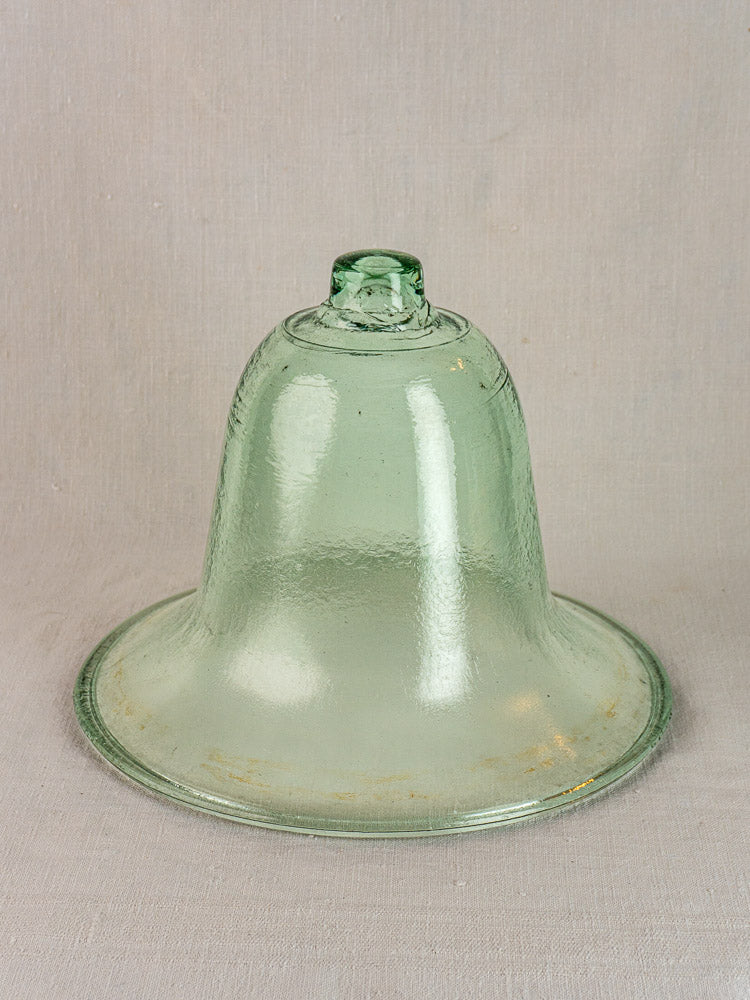 Hand-blown 19th-century French glass garden cloche with green tint and knob handle on neutral fabric background.