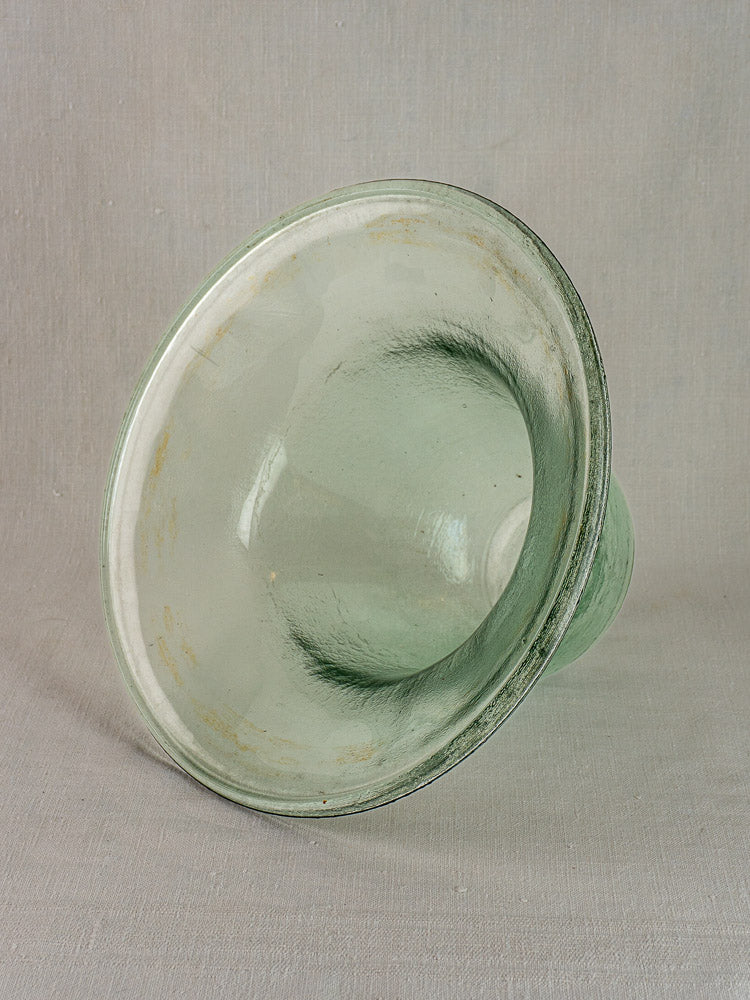 Hand-blown pale green 19th-century French glass garden cloche with wide flared rim, on neutral fabric background.