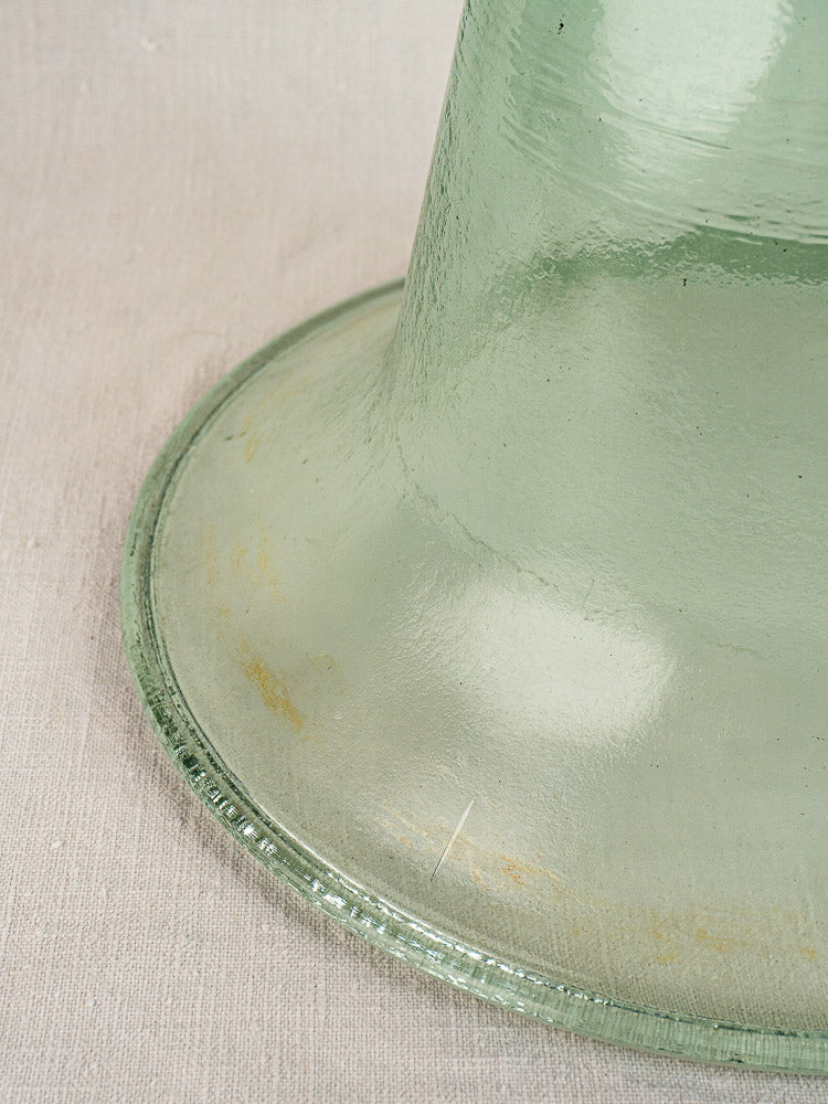 Antique French hand-blown glass garden cloche with flared base, light green, on beige textured fabric.