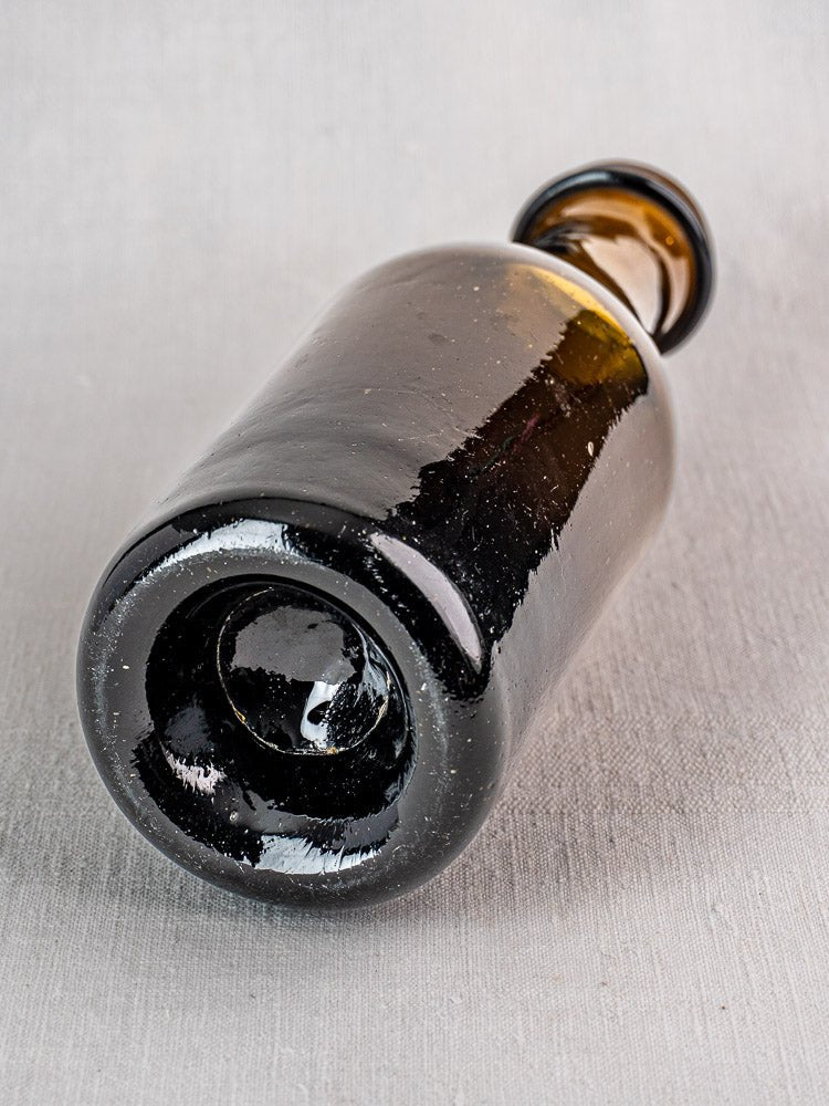 Antique French hand blown glass truffle jar resting sideways on a light gray textured surface.