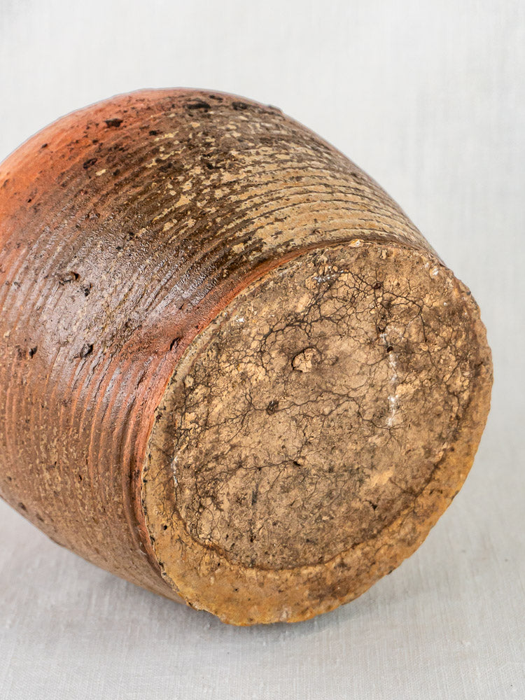 Close-up of antique French glazed terracotta jar base, rustic brown glaze, textured sides, cracked bottom.