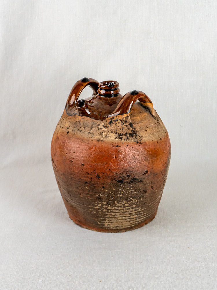 Antique French glazed terracotta oil jar with twin handles, brown body, and textured unglazed base.