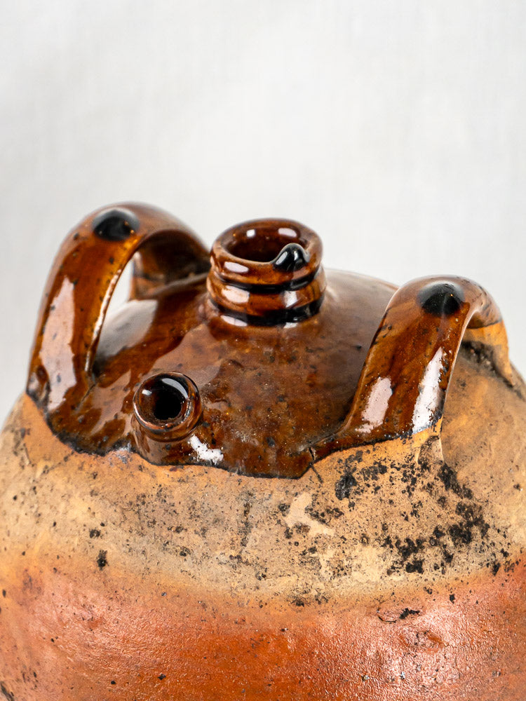 Close-up of antique French glazed terracotta oil jar with two curved handles and weathered finish.