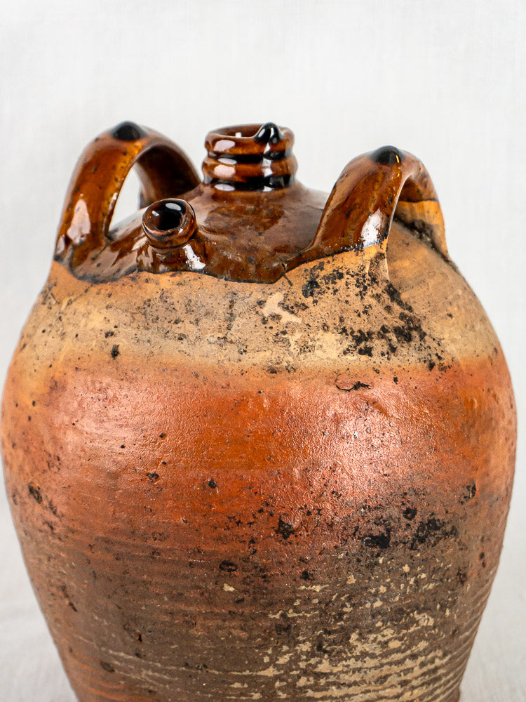 Antique French terracotta oil jar with two handles, brown and tan glazed ceramic, white background.