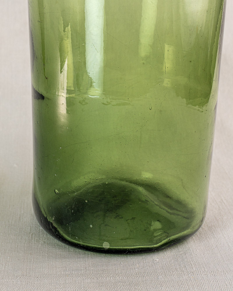 Antique French cornichon jar base, hand-blown green glass with air bubbles, on a light textured surface.