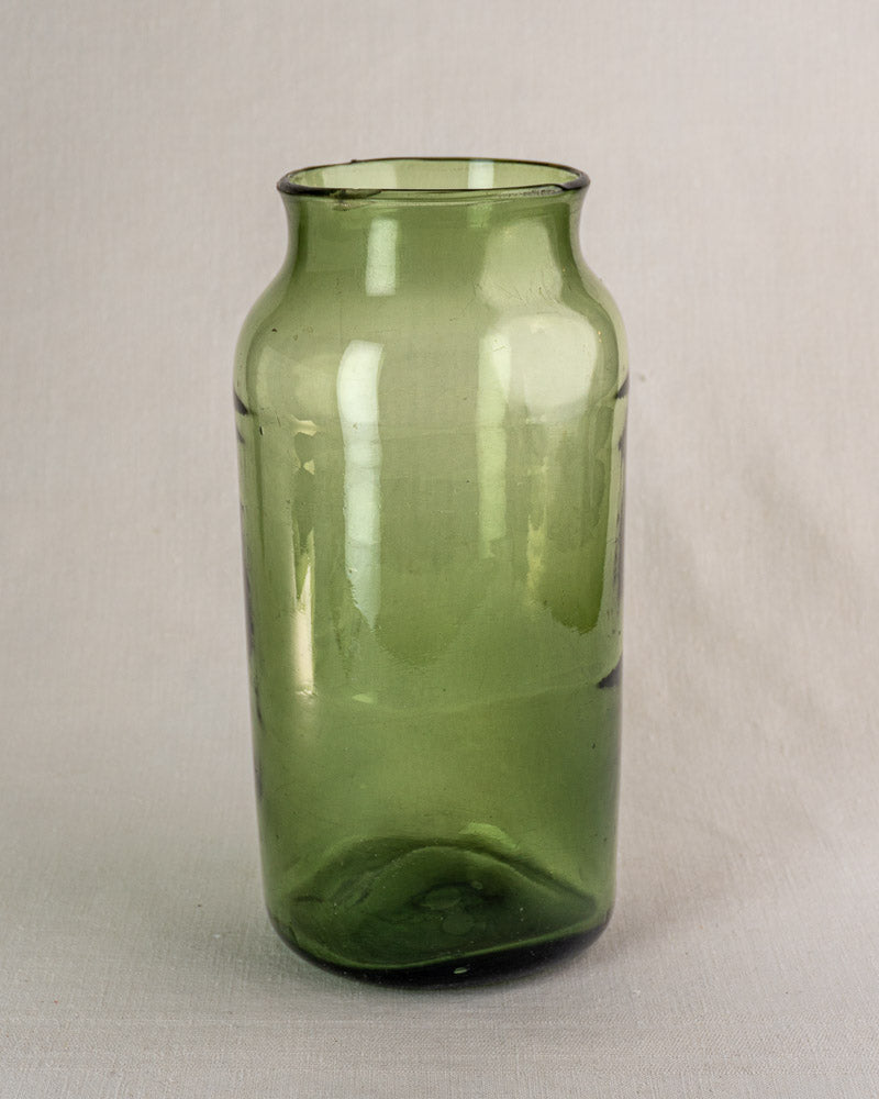 Antique French green glass cornichon jar, hand blown with flared rim, late 18th century, on light gray surface.