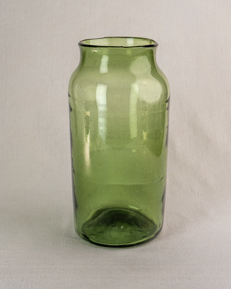 Tall hand-blown green glass French cornichon jar, late 18th century, on light beige fabric background.