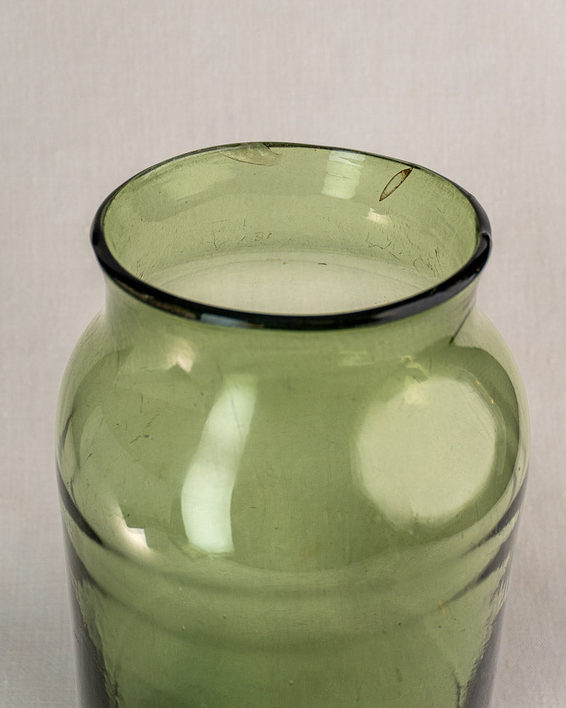 Antique French green glass cornichon jar, late 18th century, wide uneven rim, on a light background.