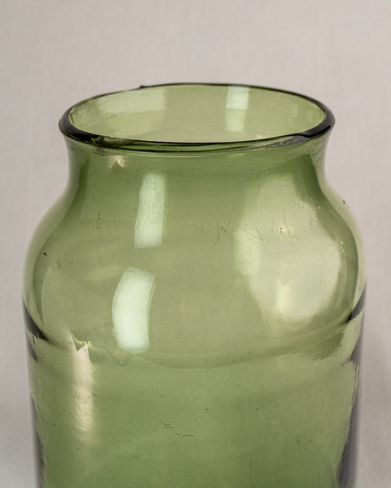 Antique French cornichon jar, late 18th century, hand blown green glass with wide opening, on beige background.