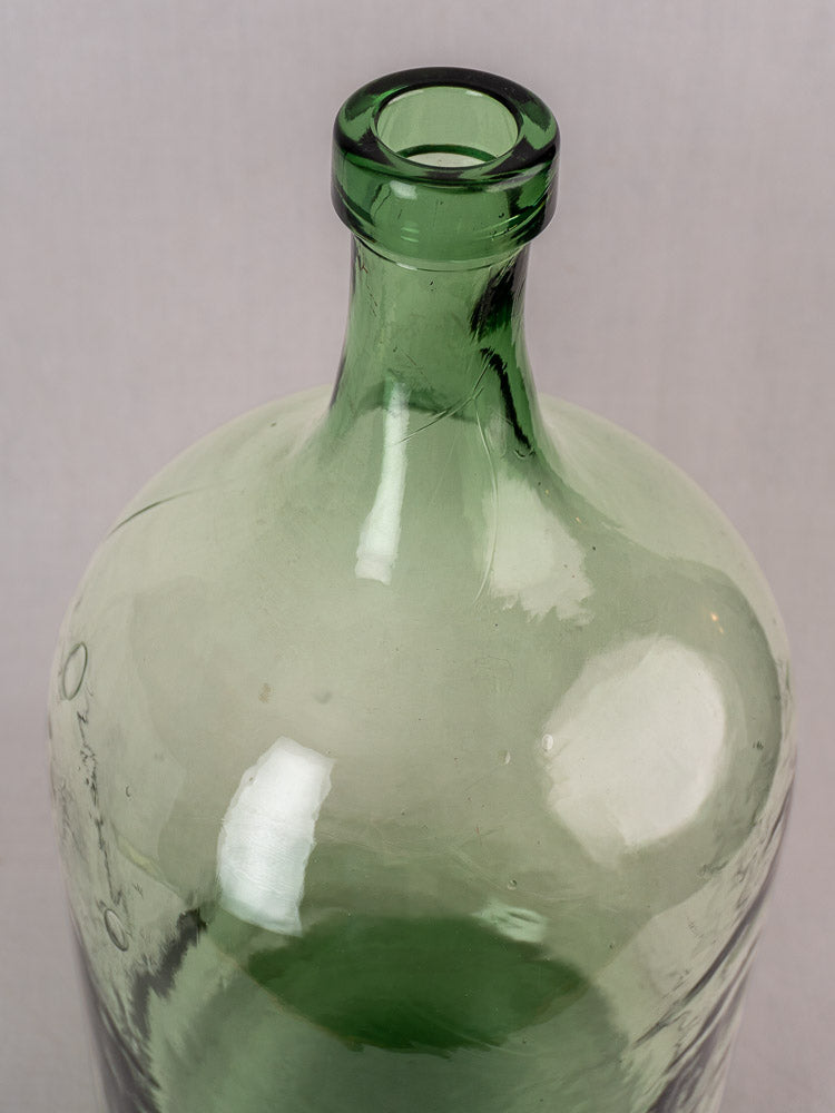 Neck and shoulder detail of an antique French demijohn, hand-blown green glass, late 19th–early 20th century, plain backdrop.