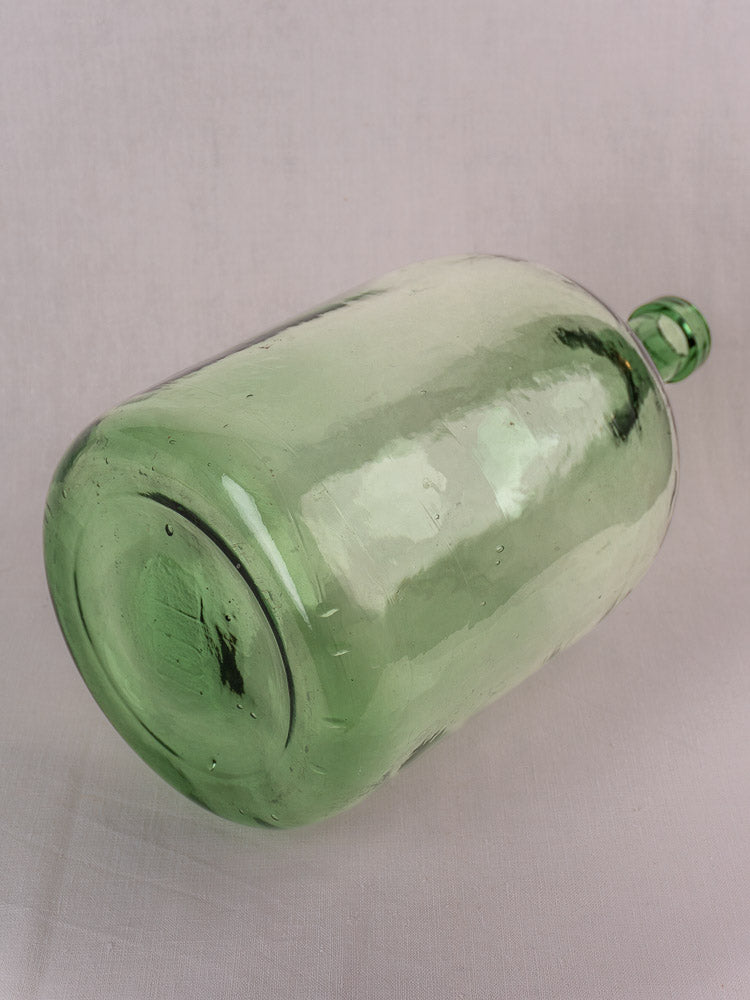 Antique French demijohn, hand blown green glass, 20L, narrow neck, textured surface on plain background.