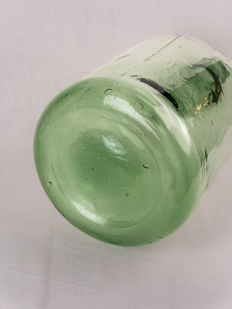 Antique French hand-blown green glass demijohn, late 19th–early 20th century, showing artisanal bubbles on light fabric.
