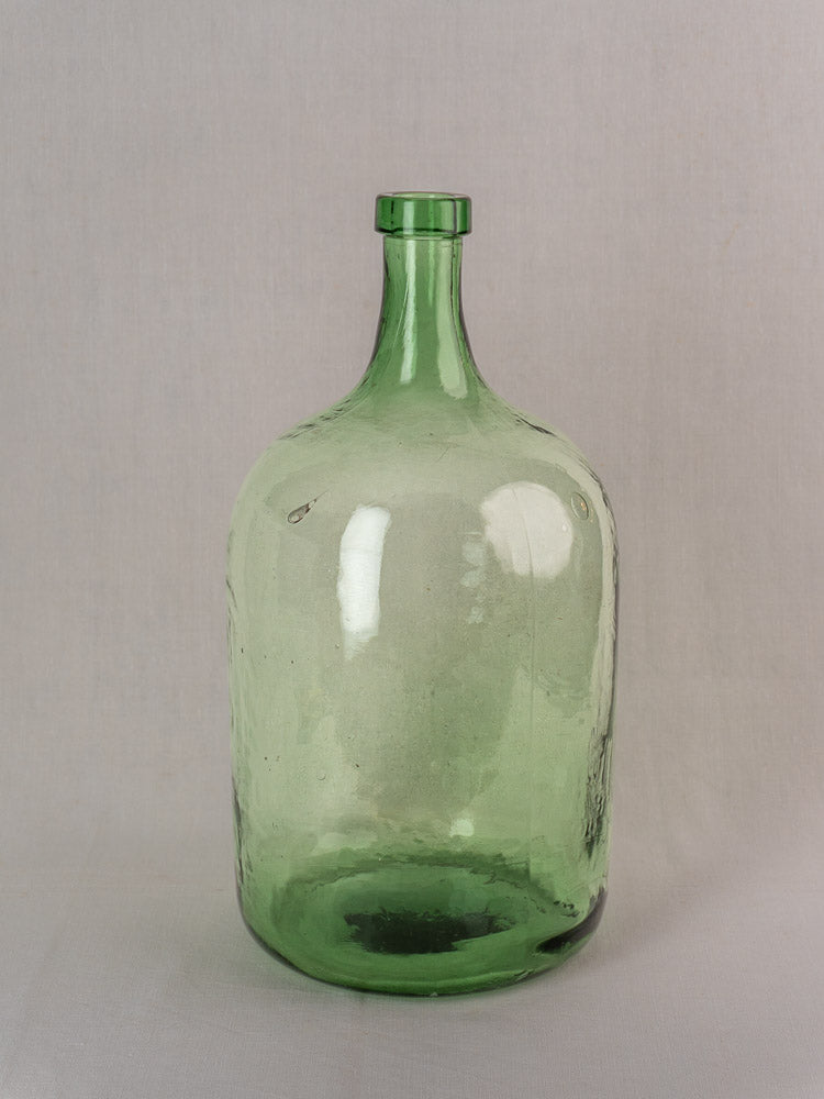 Antique French green glass demijohn, hand blown, 20L, late 19th to early 20th century, on light gray surface.