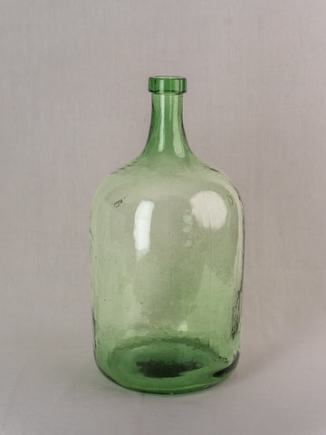 Antique French green glass demijohn, hand blown, 20L, late 19th to early 20th century, on light gray surface.