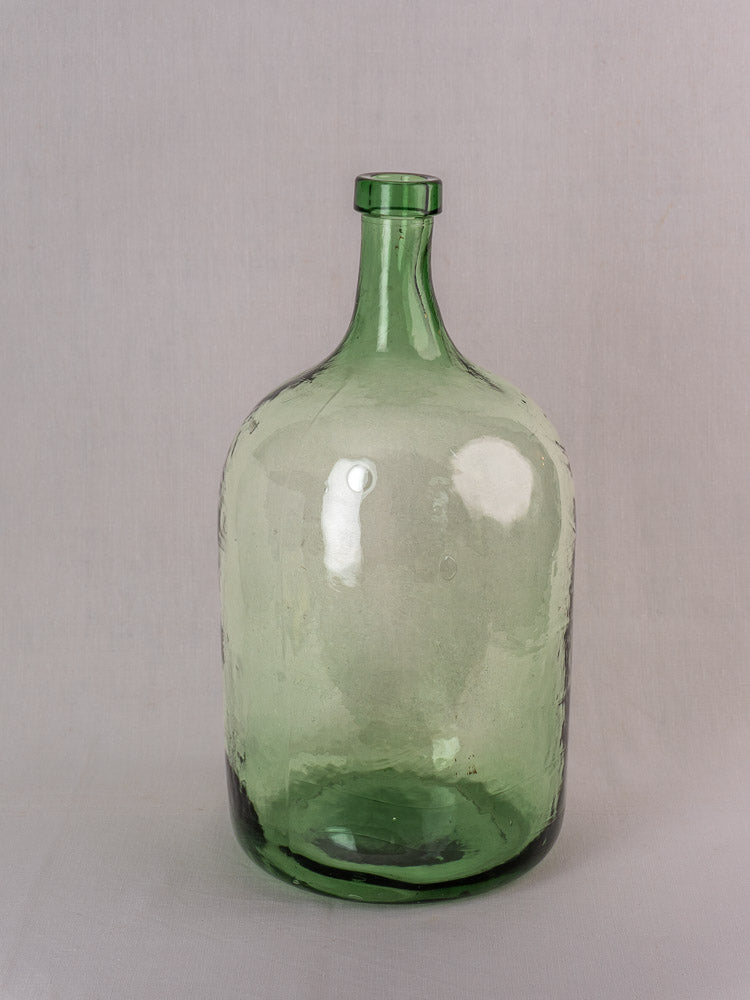 Hand-blown green glass antique French demijohn with narrow neck and rounded shoulders, set against light gray background.
