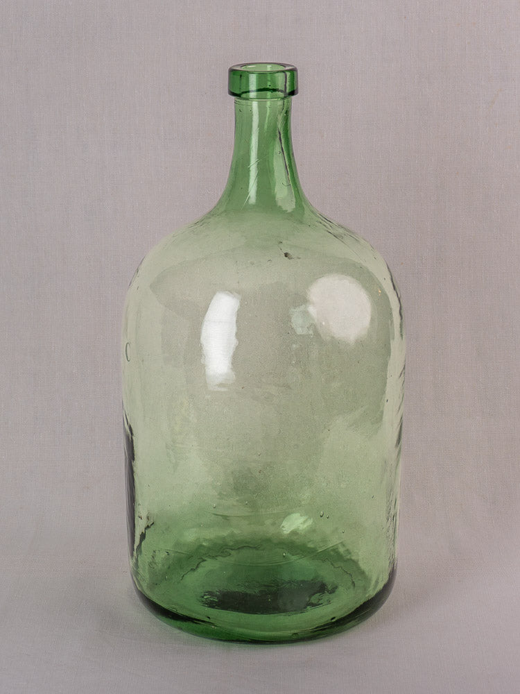 Large antique French demijohn, hand blown green glass, 20L, narrow neck and rounded body on a light gray background.