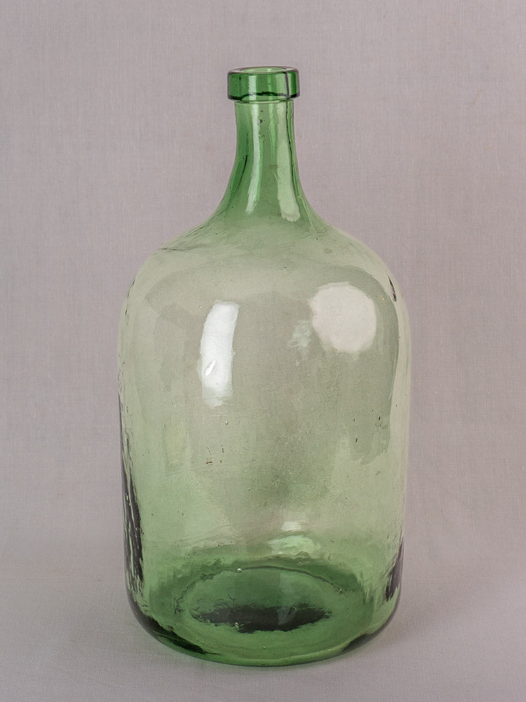 Antique French hand-blown green glass demijohn bottle with round body, narrow neck, and vintage textured finish.