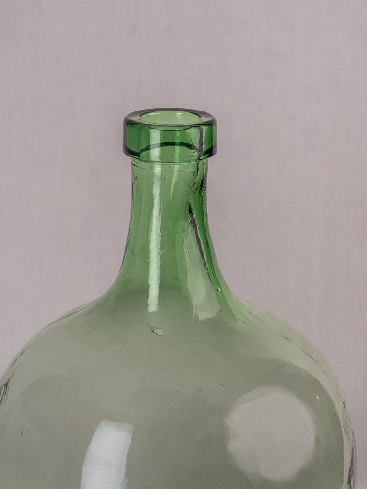 Antique French hand-blown green glass demijohn, late 19th century, round shape, air bubbles, plain light background.