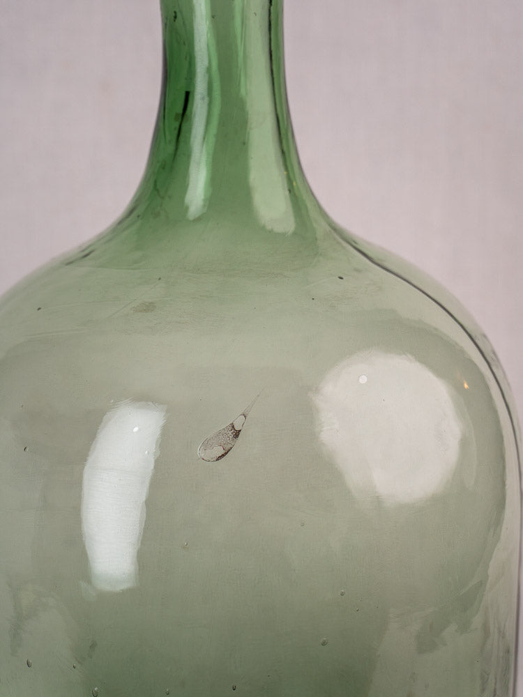 Antique French green glass demijohn, hand blown with light reflections, minor chip, neutral background.