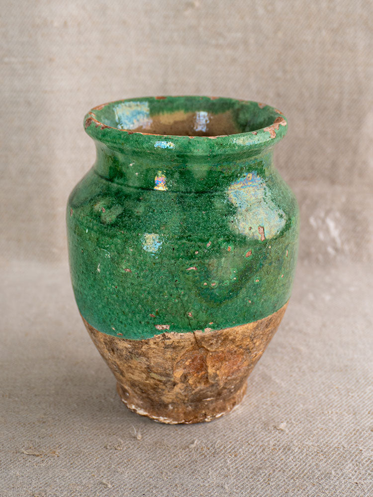 Antique French confit pot with green glazed top and unglazed brown base on a neutral fabric backdrop.