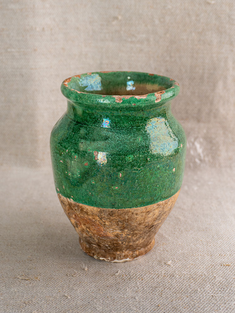 19th-century French confit pot with green glazed terracotta top, unglazed base, on neutral textured fabric background.