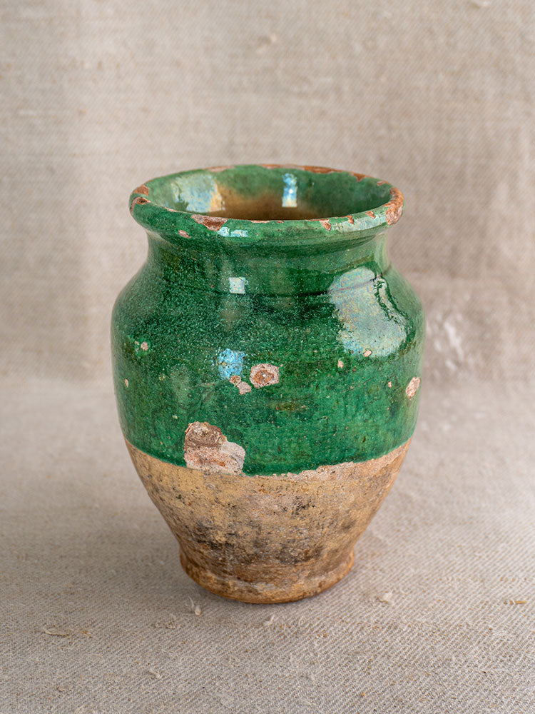 Antique French confit pot with green glaze top and unglazed beige base on textured beige fabric.