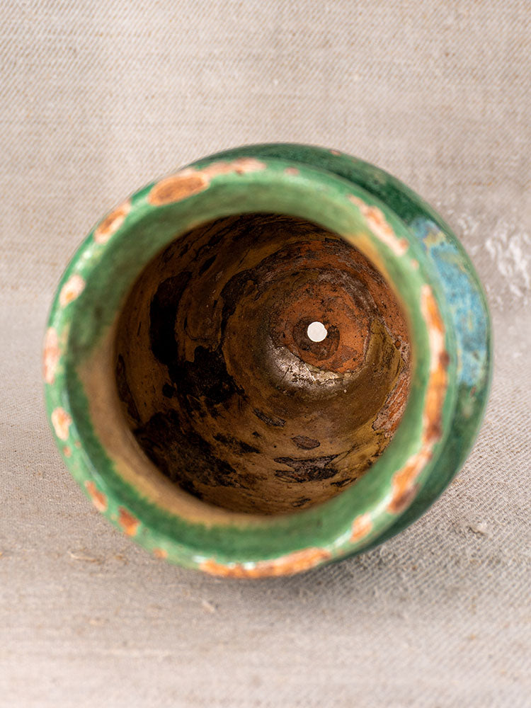 19th-century French confit pot with weathered green glaze, shown sideways to display the worn interior and drainage hole.