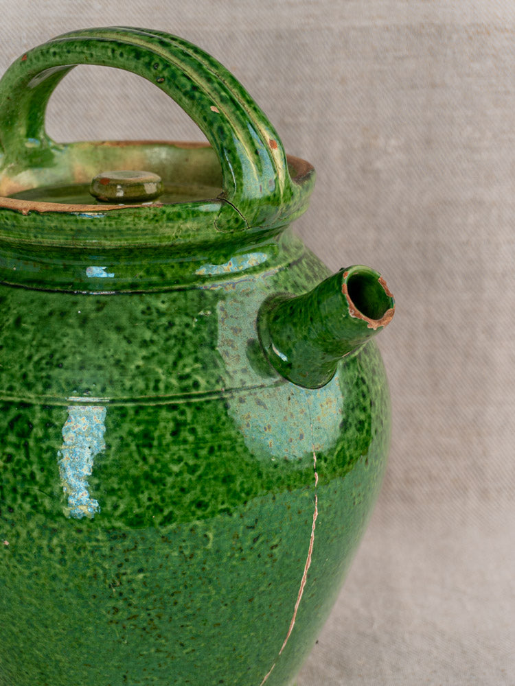 Antique French green glazed cruche Orjol water jug with curved handle, spout, base crack on neutral textured fabric.