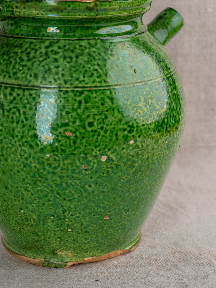 Antique French green glazed cruche Orjol with handle and rustic chips, early 20th century, on neutral fabric.